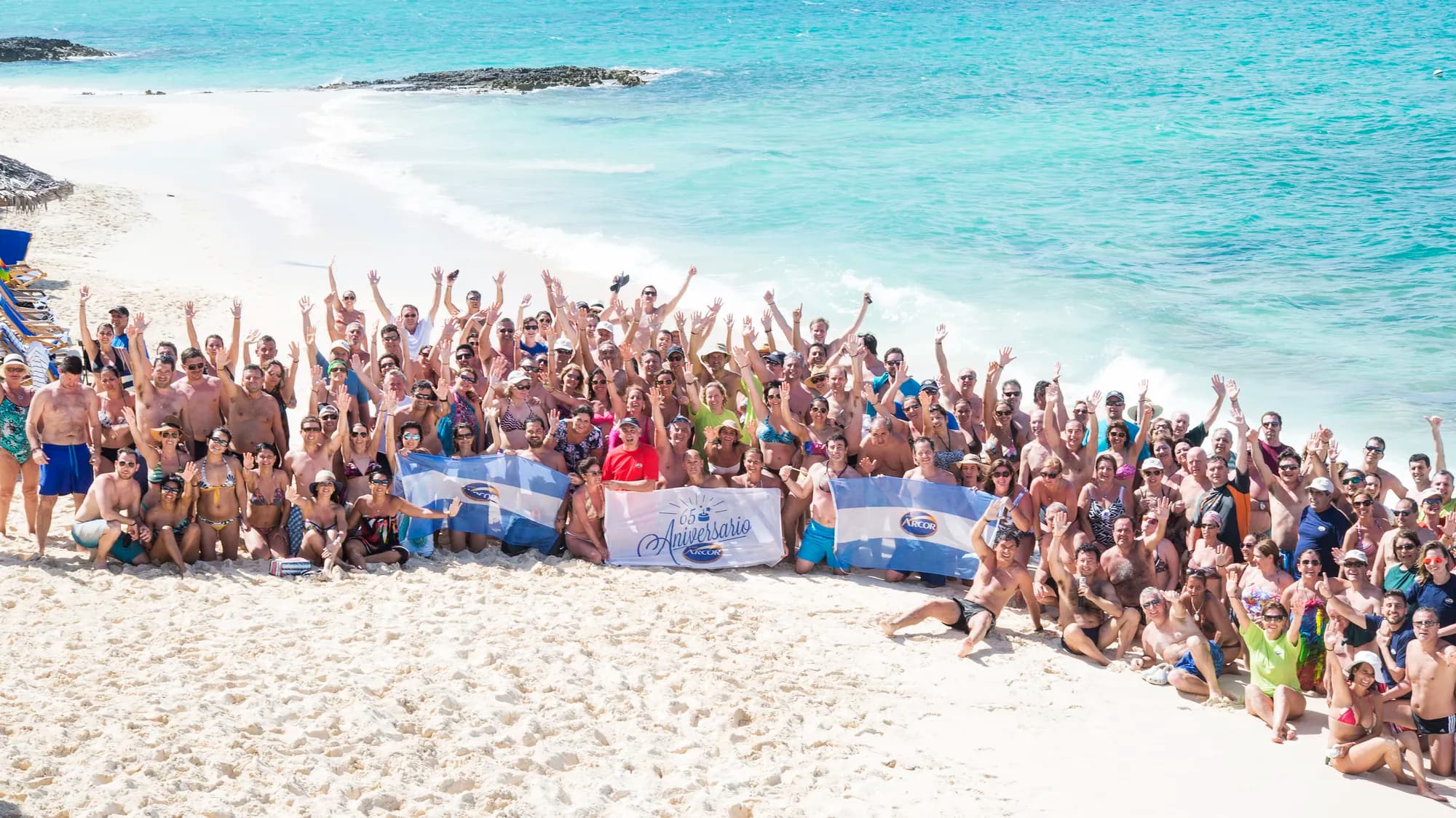 AV Business & Communication incentive group celebrating with raised arms on a white-sand beach
